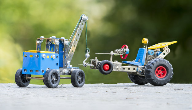 Toy tow truck lifts car, both built with small pieces of metal and plastic. Roadside assistance concept.