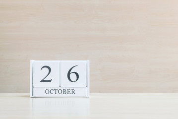 Closeup surface white wooden calendar with black 26 october word on blurred brown wood desk and wood wall textured background with copy space , selective focus at the calendar