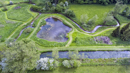 Aerial view of green lush fields surrounded by ponds, streams, trees, shrubs, walking paths in summer English countryside