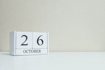 Closeup white wooden calendar with black 26 october word on blurred white wood desk and cream color...