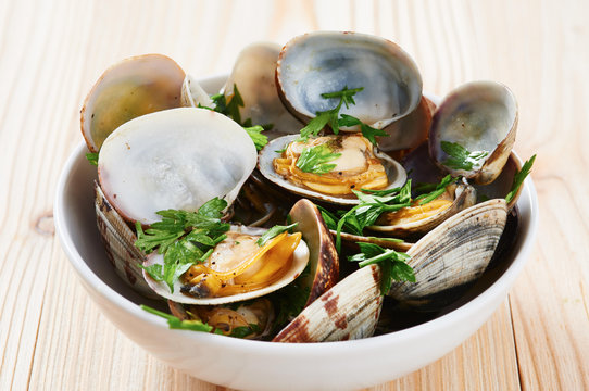Steamed clams in white bowl on wooden table