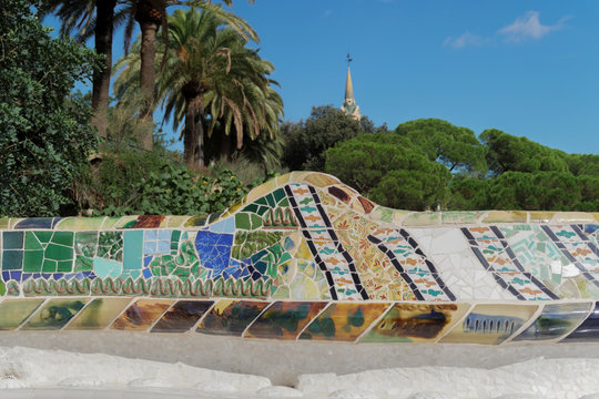 Barcelona, Spain Park Guell mosaic seating at Nature Square Placa de la Natura.
Mosaic seating area with multi-coloured tiles at at Nature Square. Gaudi House Museum rooftop visible in background

