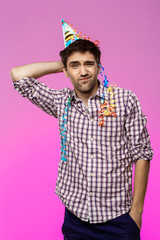Fototapeta premium Displeased tired man at birthday party over purple background.