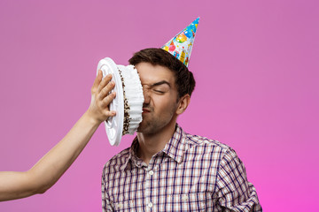 Man with cake on face over purple background. Birthday party.