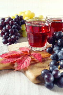 Two glasses of grape juice with ice and black and green grapes