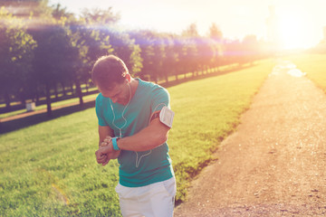 Athlete checking time results at his smart watches on the wrist after workout in the park, lens flares