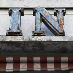 Faded rusting word IN above an old retail shop canopy