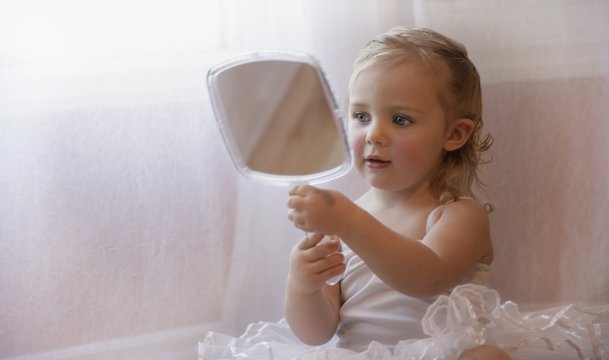 Little Girl Looking At Herself In A Hand Mirror