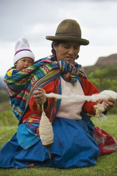Cuzco, Peru; Woman Spinning Alpaca Wool While Carrying Her Baby On Her Back