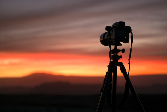 Camera set on a tripod aimed at a silhouette of a landscape during sunset