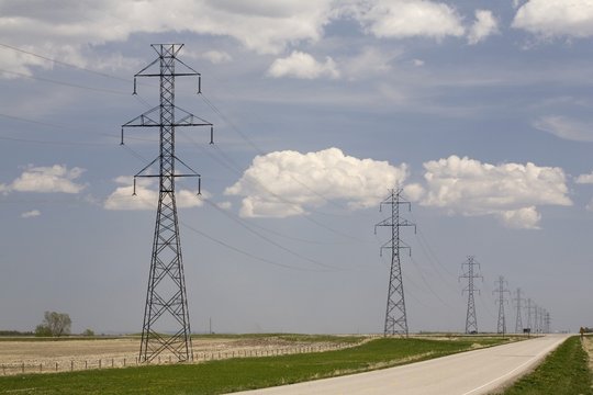 Metal Power Lines In A Row Running Along A Road With A Blue Sky And Clouds; Calgary, Alberta, Canada