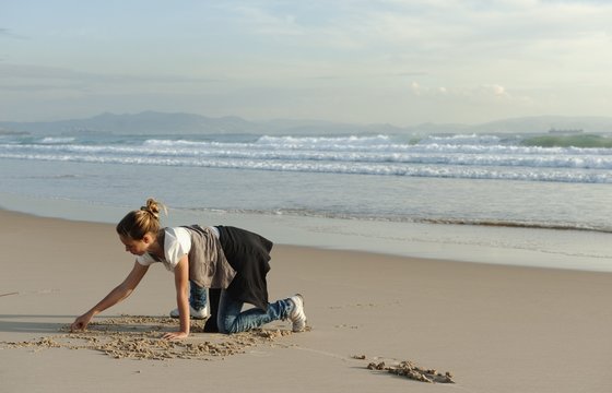 A Girl Drawing In The Sand At Los Lances Beach Along Costa De La Luz; Tarifa, Cadiz, Andalusia, Spain