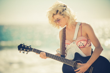 Cute blonde woman playing guitar at the beach