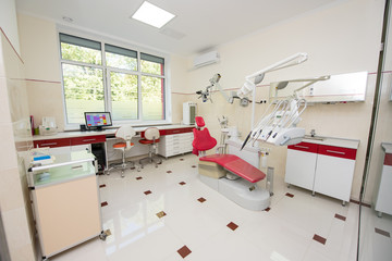 Dental clinic with modern dental units, chairs, equipment, tools and microscope used by dentists. Dental office in red and white colors. Stomatology