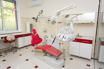 Dentistry. Dental office with modern dental units, chairs, equipment, tools and microscope used by dentists. Cabinet in red and white colors