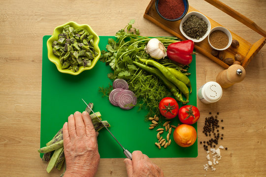 Cooking vegetables meal for vegetarians, hands cutting green beans with knife. Menu for healthy lifestyle, ingredients for cooking with spices in kitchen.
