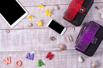 Overhead of a essentials objects in a fashion blogger. Top view of fashion python snakeskin handbag, word "woman", smartphone, tablet pc, shells. Plumeria frangipani flowers. Wooden background.
