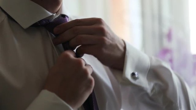 A picture of a groom fixing a fine tie carefully, neat white shirt on