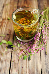Herbal tea in a transparent glass mug and forest herbs on a wooden surface of a table. Tea from autumn herbs. Phytotea
