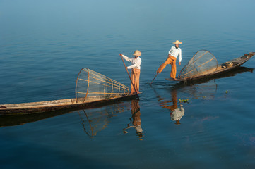 Burmese fisherman on bamboo boat catching fish in traditional way with handmade net. Inle lake,...