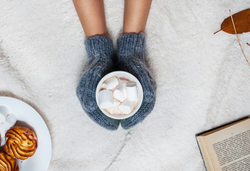 Hands in knitted mittens holding hot chocolate with marshmallow