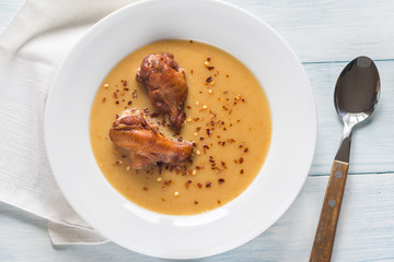 Portion of pea cream soup with smoked chicken wings