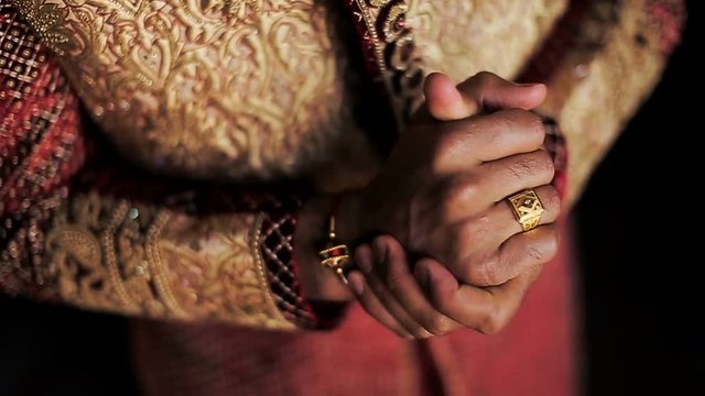Indian man holds his hands together standing in wedding suit