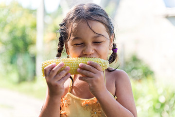 Child in the garden - lovely girl eating corn on the cob (GMO free).