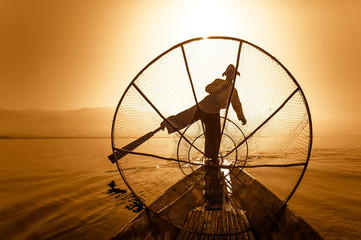 Burmese fisherman on bamboo boat catching fish in traditional way with handmade net. Inle lake, Myanmar (Burma) travel destination