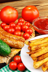 Homemade fast food, portion of french fries, ketchup, grilled sausages and cherry tomato on wooden board.