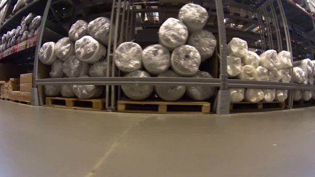 POV shopping cart moving fast in furniture warehouse store between shelves with cardboard boxes and packed mattresses
