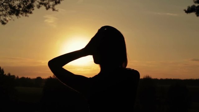 Silhouette of woman putting on the headphones, listening to music and dancing in the forest. Sunset light, sun lens flares, golden hour. Relax, nature and joyful concept