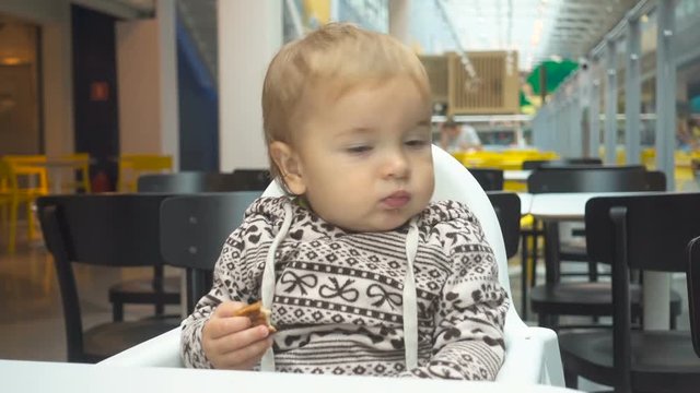 One year old child eats in a cafe. Baby boy sitting at a table in a cafe with Cake.