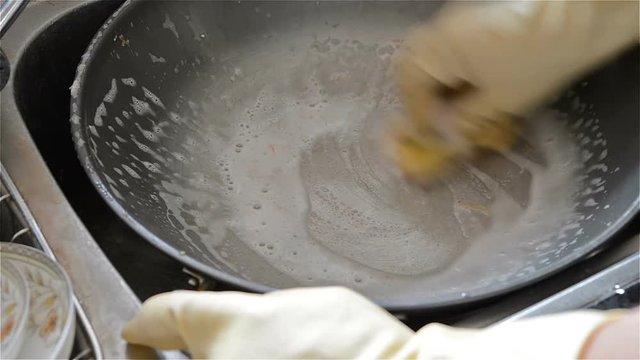man washing a pan in the kitchen sink with soapy sponge