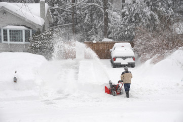 man removing snow on the driveway of the house by snow blower