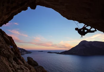 Rolgordijnen Male climber climbing along roof in cave at sunset © Andrey Bandurenko