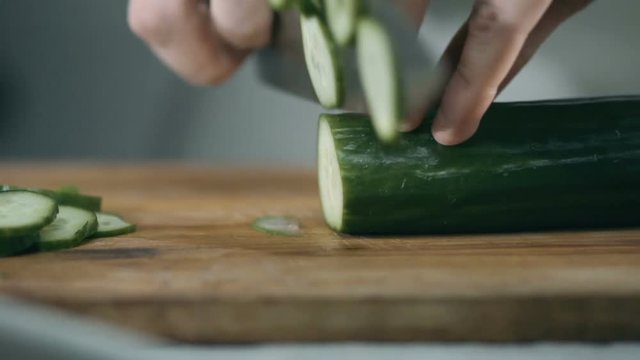 Chef cuts the cucumber with a sharp knife on a wooden board