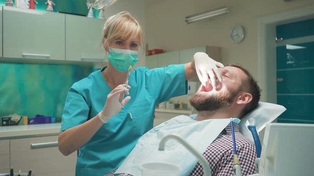 Female dentist examining an drilling patient's tooth. Visit is in proffessional dental clinic. He is sitting on dental chair. He is young and has beard. Dolly and steadicam shot.
