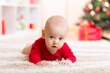 Cute baby lying on tummy in front of Christmas tree