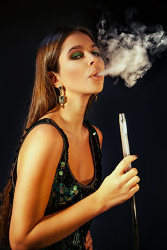 Young, beautiful girl in club dress and perfect make up smoke a