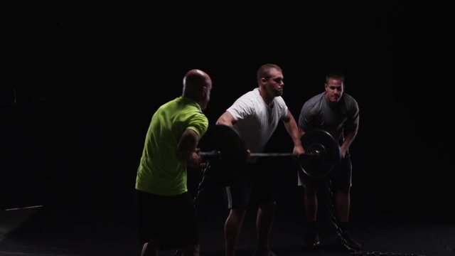Athlete training, two men help another man lift weights.