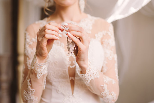 closeup of a bride in white lace wedding dress hold her earrings