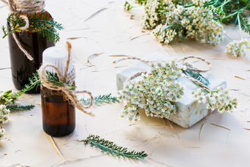 Milfoil flower, yarrow essential oil in glass bottles on a light table. Used in medicine, cosmetics and aromatherapy. Fresh flowers, green leaves and a piece of soap. - 124214145