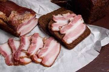 Puff smoked bacon with rye black bread on the packaging paper. V
