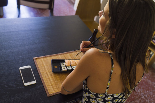 Happy woman using mobile at table with sushi and drink