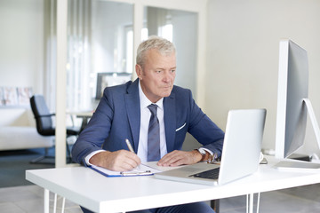 Fototapeta na wymiar Financial businessman at work. Shot of a senior financial manager working at office in front of laptop and and doing some paperwork. 