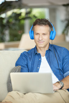 Casual Man With Laptop At Home. Shot Of A Middle Aged Casual Man Listening Music With Headphone And Using Laptop While Relaxing After Work.