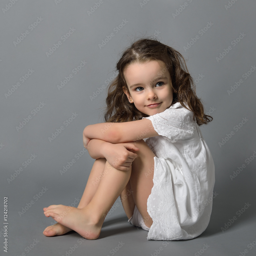 Wall mural sweet little happy girl in white dress, studio portrait over gra