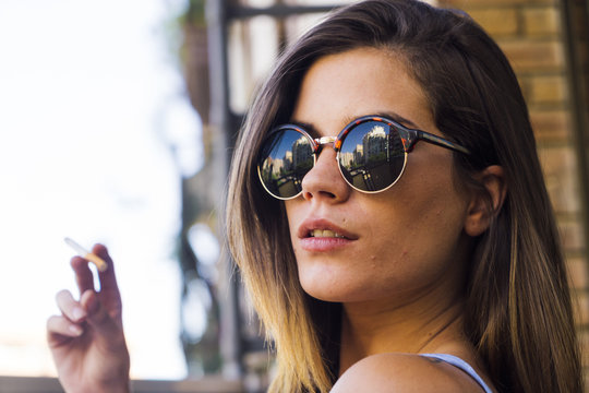 Beautiful young girl in sunglasses smoking cigarette