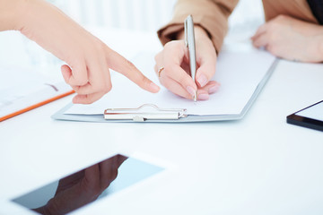 Two business women in a meeting discussing information and taking notes as they work together as a team, close up view of their hands.